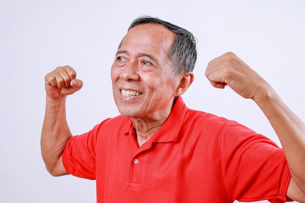A smiling older man in a red shirt, steady and warm in afternoon light.