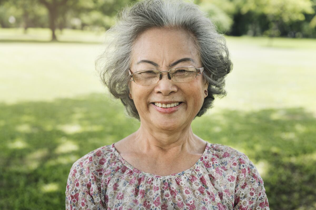 Una señora mayor sonriendo al aire libre, recibiendo el aire fresco y la luz de la mañana.